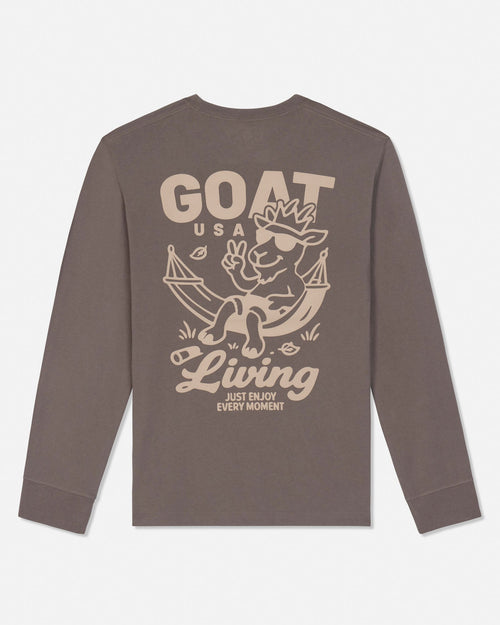 A long-sleeve crewneck t-shirt in a muted brownish-gray color, featuring a large beige graphic print on the back with a cartoon goat in a hammock and the text 'GOAT USA Living JUST ENJOY EVERY MOMENT'.