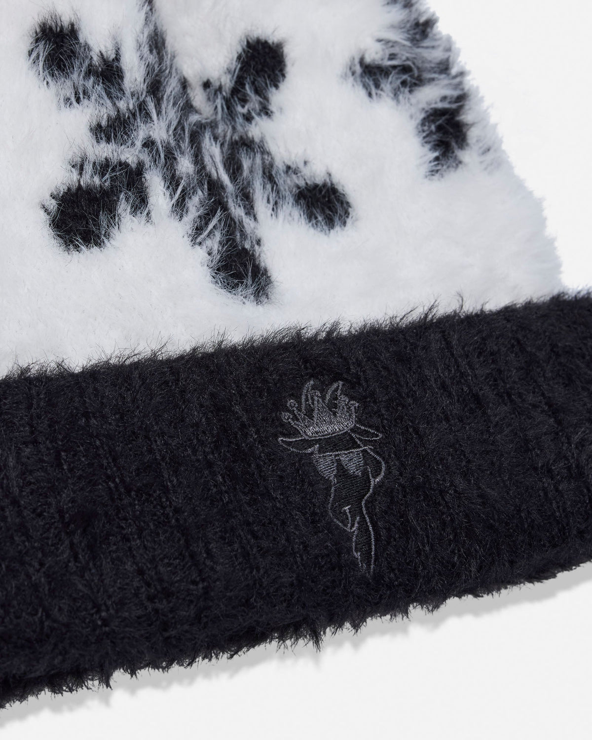 Close-up of a black and white fuzzy beanie with a ribbed black cuff and a small embroidered logo.