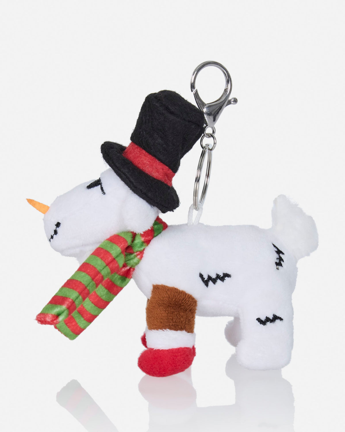 A plush white goat character keychain decorated with a black top hat, red band, green and red striped scarf, red boot, and orange horn, attached to a silver metal clasp on a light gray background.