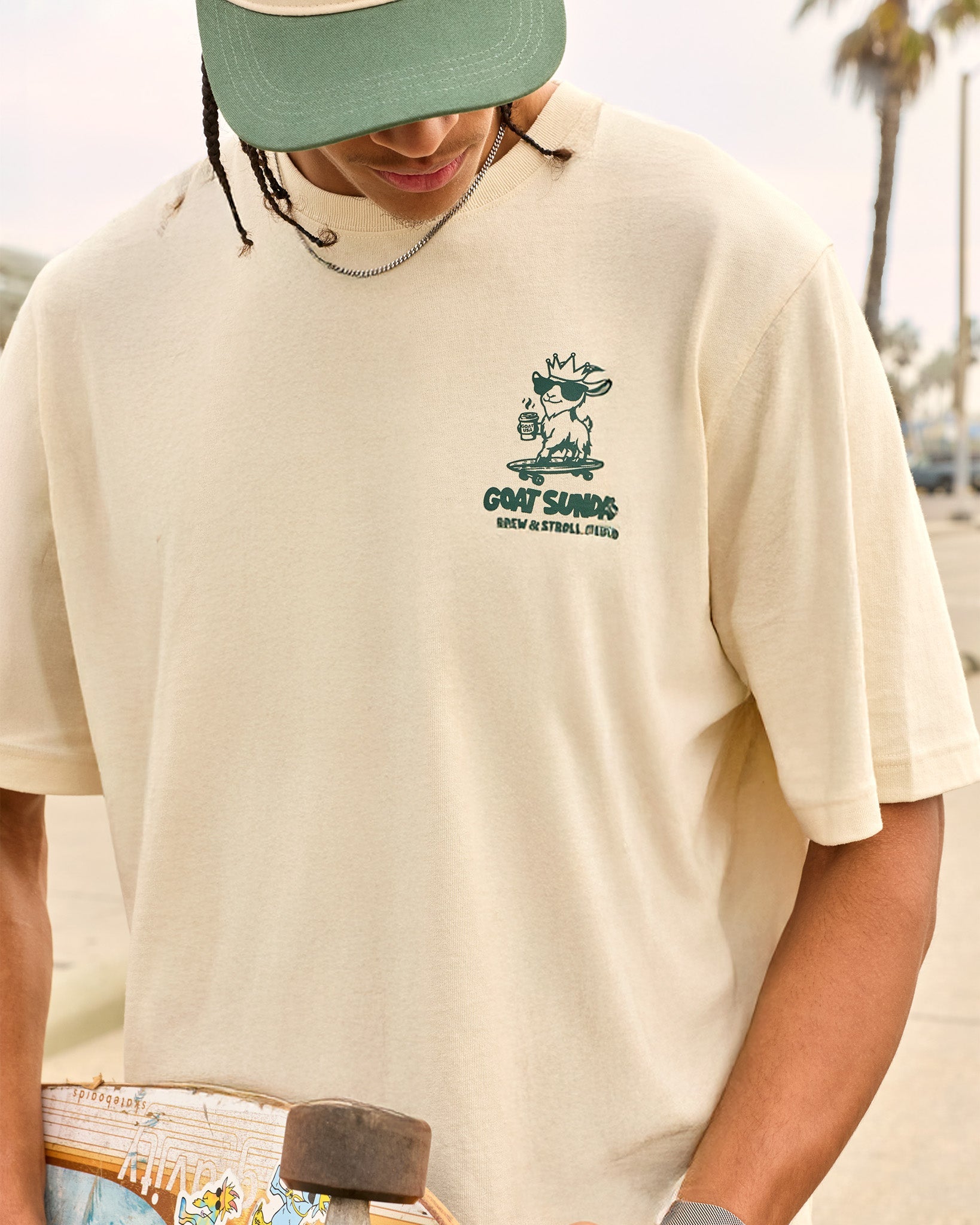 Person wearing a beige t-shirt with a graphic design, standing outdoors with palm trees in the background.