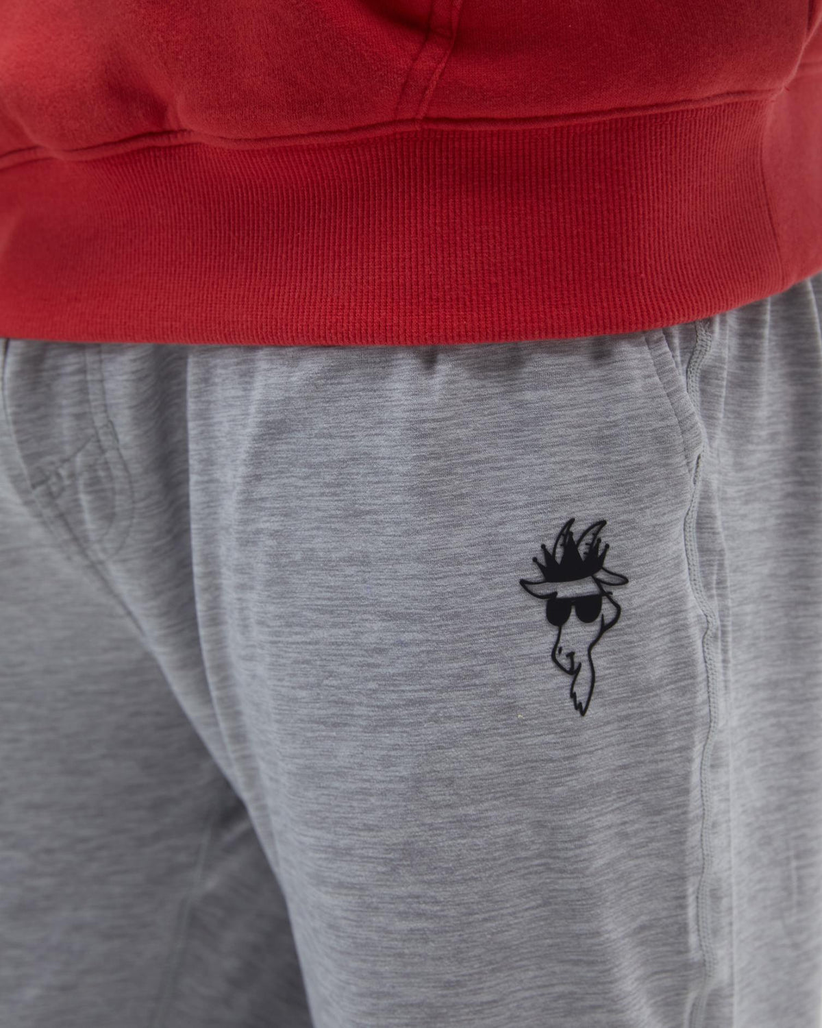 Gray sweatpants with a black embroidered design on the leg, worn with a red hoodie.