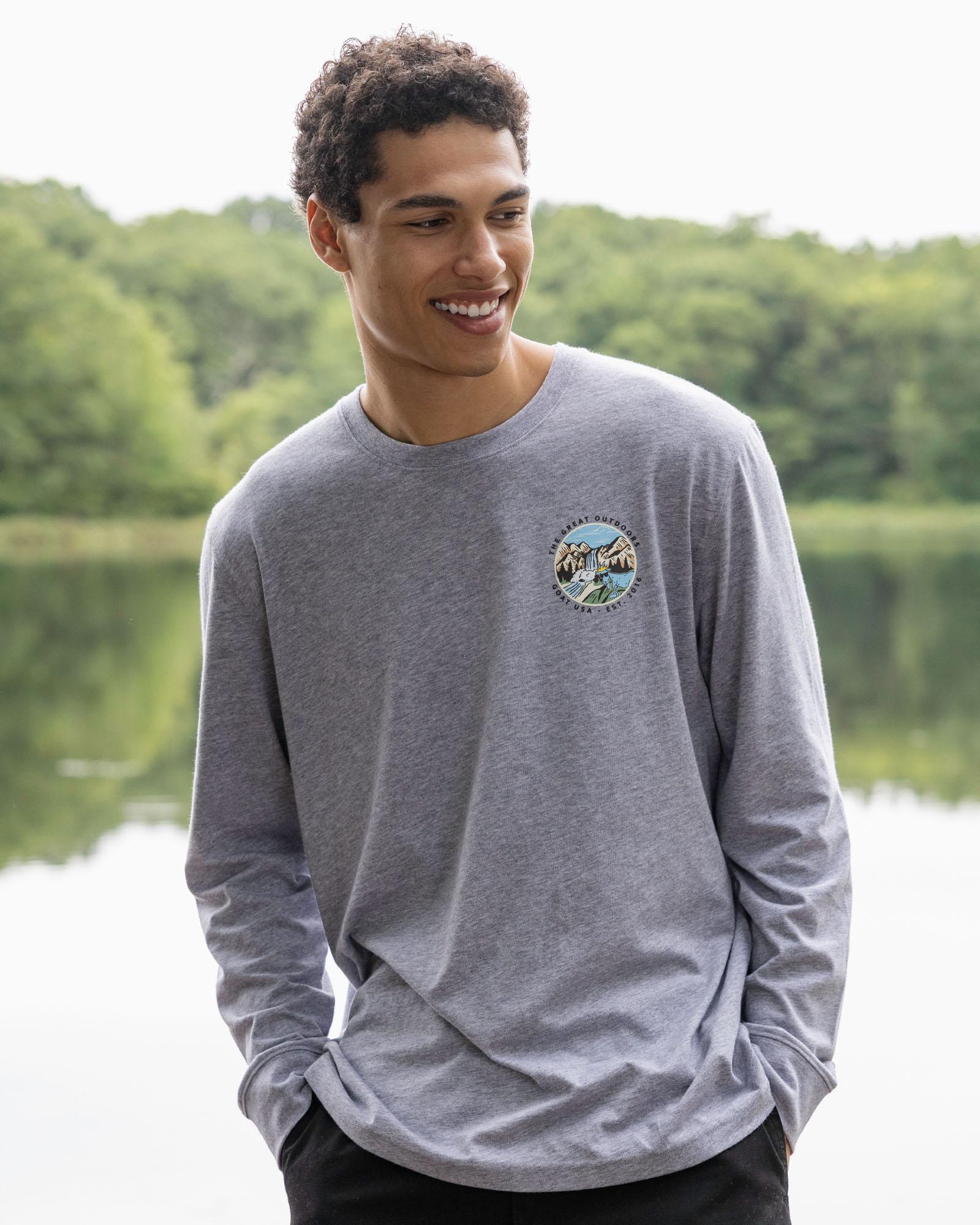 Man wearing a gray long-sleeve shirt with a logo standing by a lake.