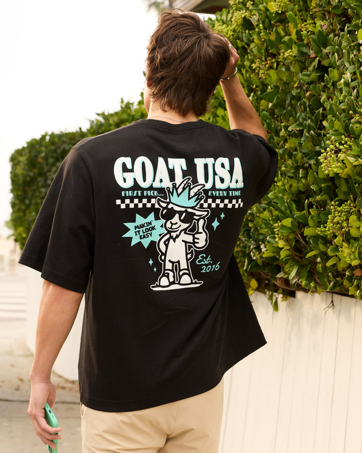 Person wearing a black 'GOAT USA' t-shirt with a graphic design on the back, standing outdoors.