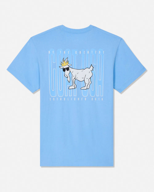 A light blue short-sleeve t-shirt with a graphic on the front featuring a white goat wearing sunglasses and a gold crown, set against a white background with vertical text.