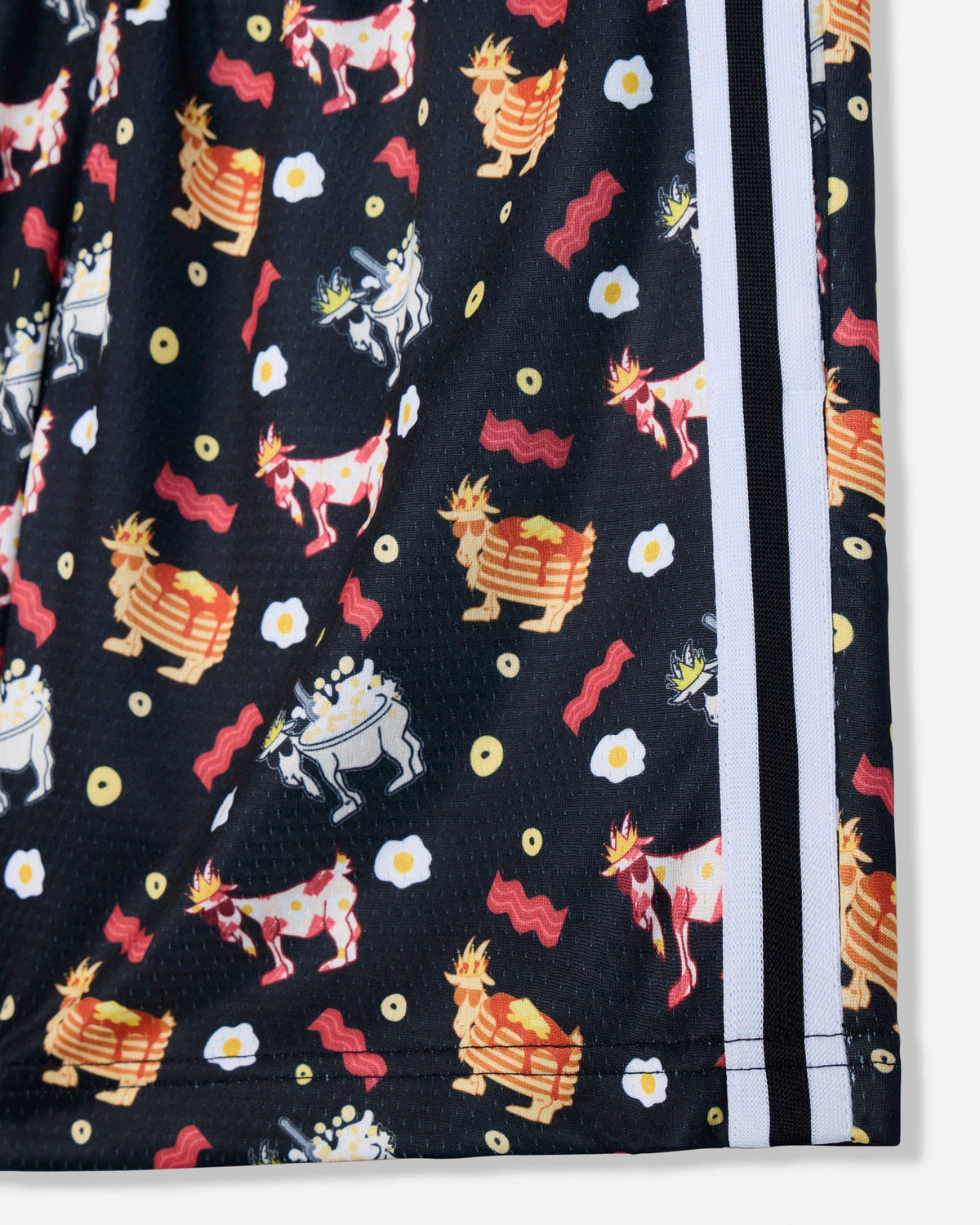 Close-up of a black athletic shorts leg featuring a colorful cartoon print of goats, eggs, and bacon, with white side stripes.