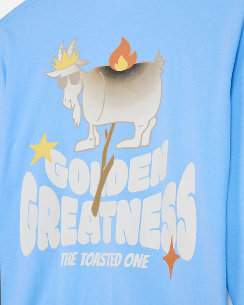 A close-up of a light blue long-sleeve shirt featuring a graphic print of a goat wearing a golden crown and sunglasses, with a flame on its back, and the text 'GOLDEN GREATNESS THE TOASTED ONE'.