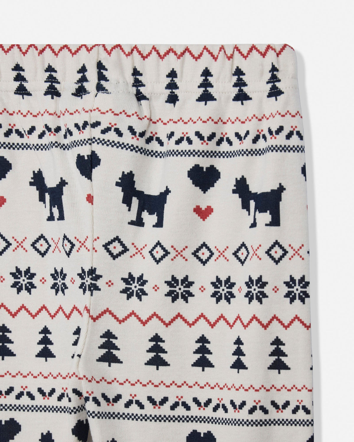 Close-up of knit pajama pants with a Christmas fair isle pattern featuring black goat silhouettes, red and navy trees, and snowflakes on an off-white background.