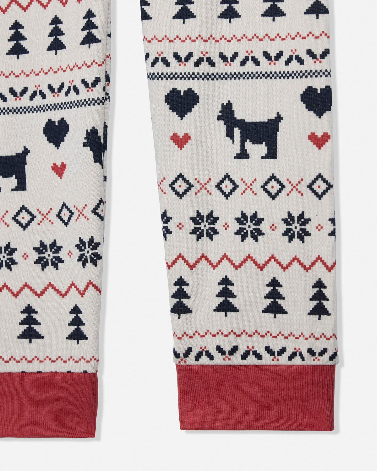 Close-up of a pair of knit pants or pajama legs with a Christmas-style pattern. The fabric is off-white with navy blue and red motifs, including trees, hearts, diamonds, and silhouettes, with solid red cuffs.