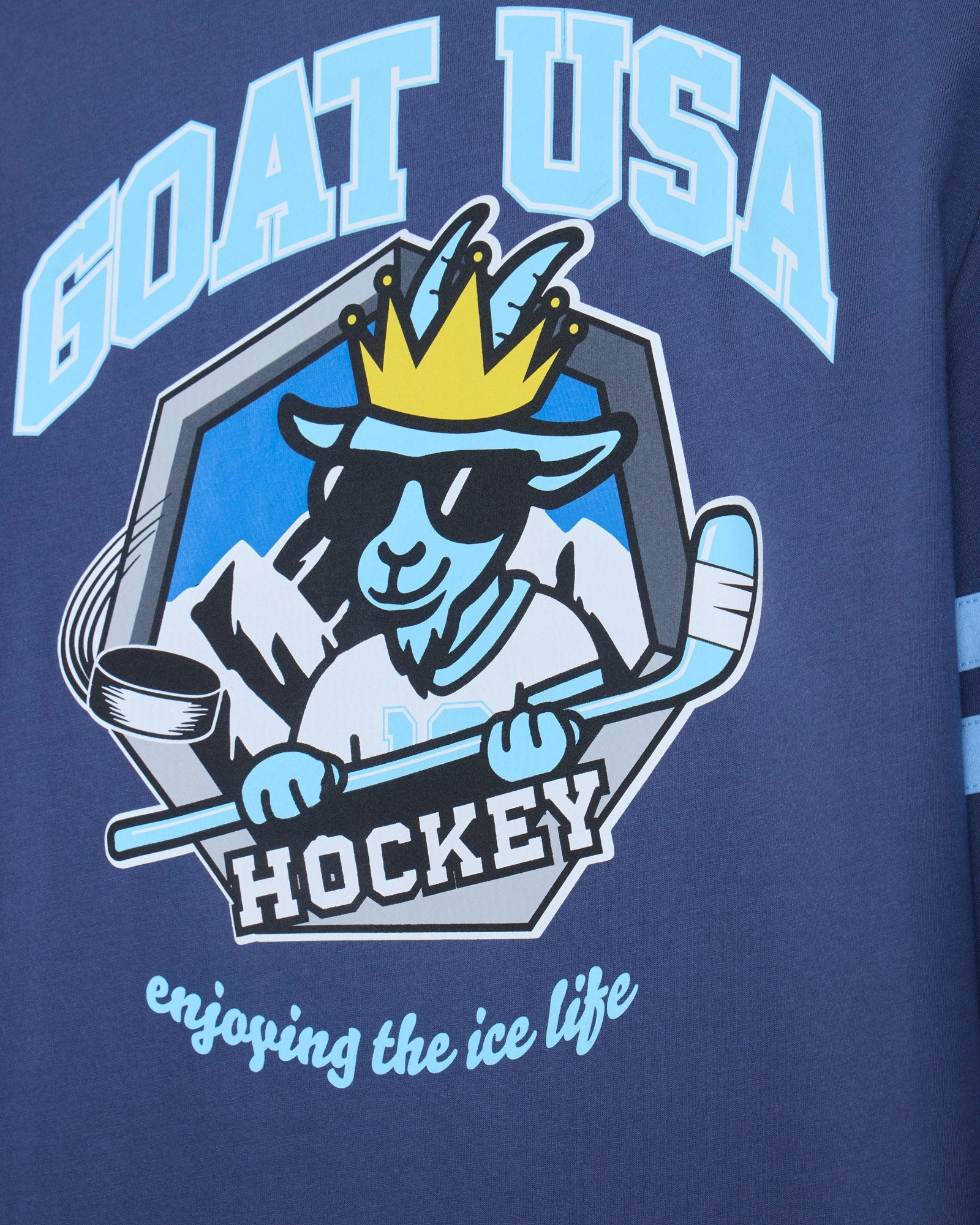 Close-up of a navy blue garment featuring a large 'GOAT USA HOCKEY' graphic with a stylized goat mascot wearing a crown and sunglasses, plus the phrase 'enjoying the ice life' in light blue script.
