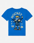 A royal blue short-sleeve t-shirt with a large graphic on the back featuring a cartoon ice hockey player wearing a gold crown and sunglasses, with the word 'HOCKEY' printed above in cream.
