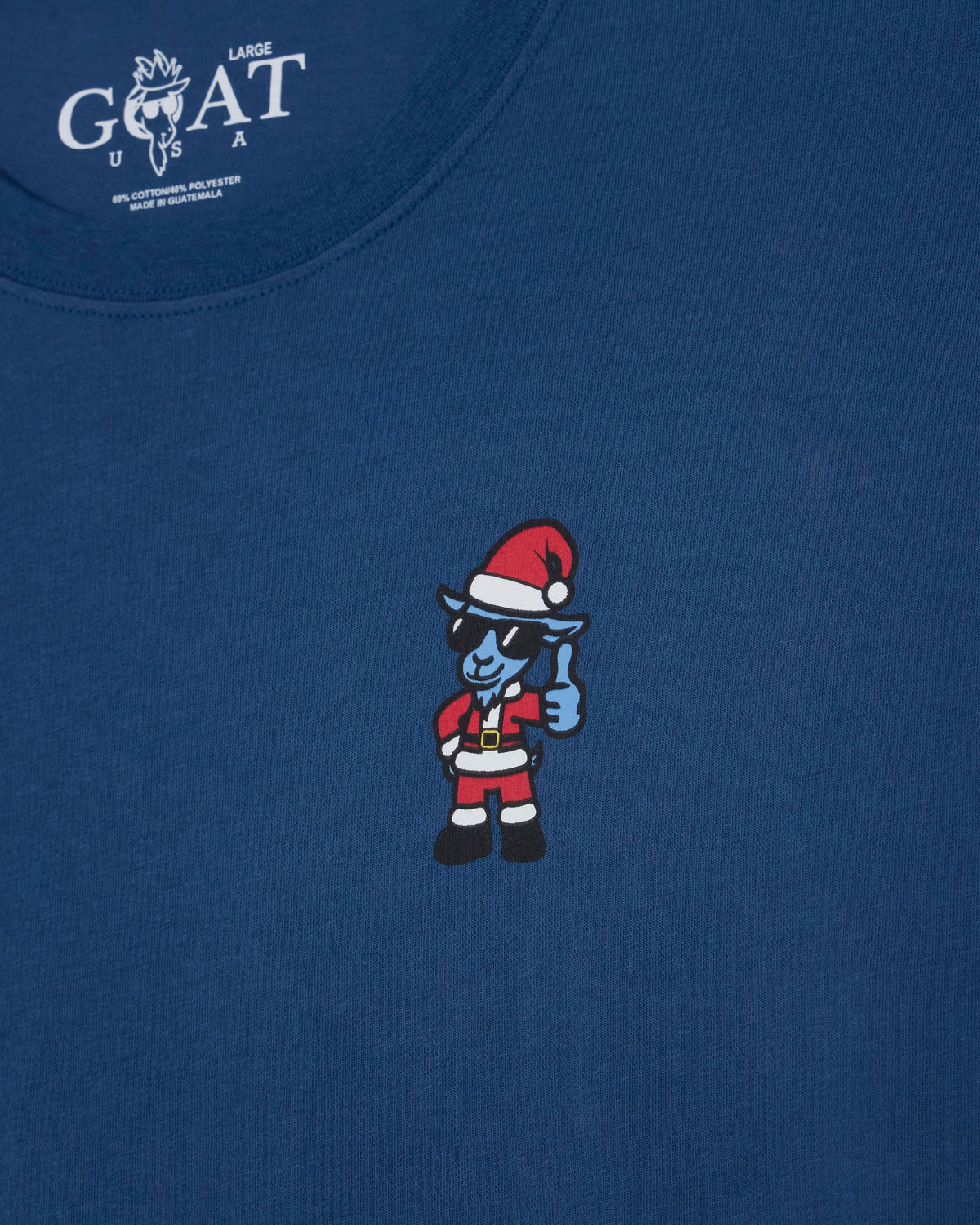 A close-up of a navy blue t-shirt featuring a small cartoon graphic of a blue goat in a Santa hat and sunglasses giving a thumbs-up on the chest. The inner neck label shows the brand 'LARGE GOAT USA'.