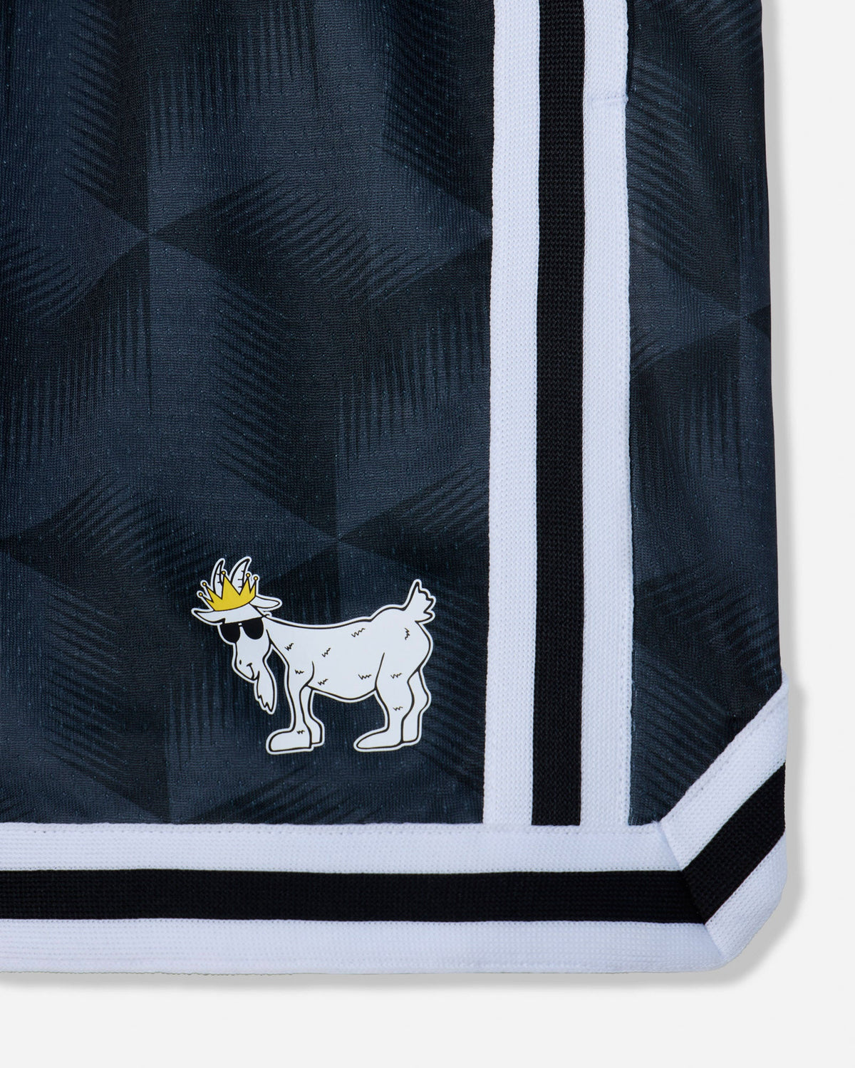 Close-up of a black patterned garment corner with a white and black striped border and a small white goat logo wearing a yellow crown.