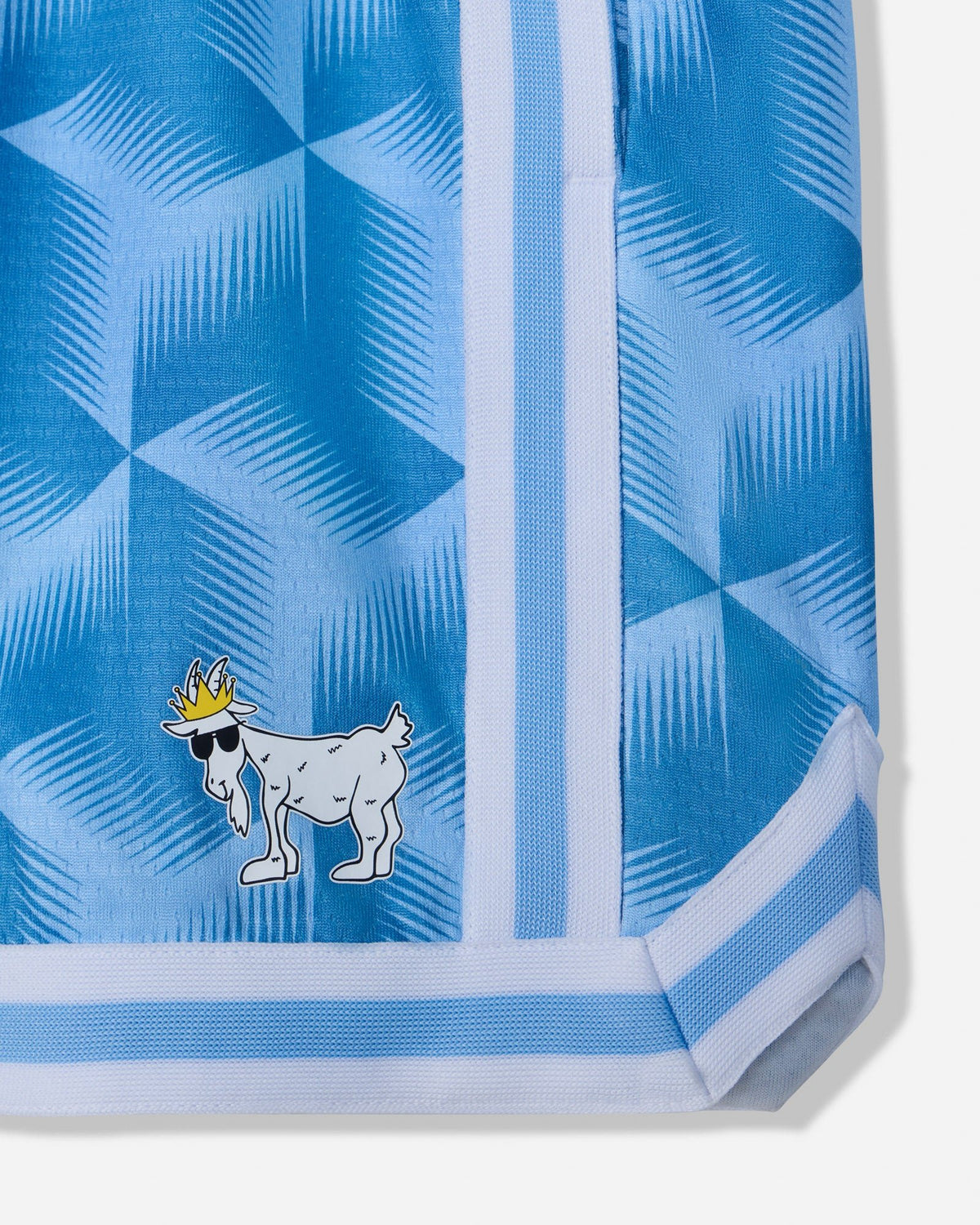 Close-up of a light blue patterned garment, likely shorts or a skirt, featuring a white and blue geometric design, a vertical white stripe, and a small cartoon goat wearing a gold crown near the lower left.