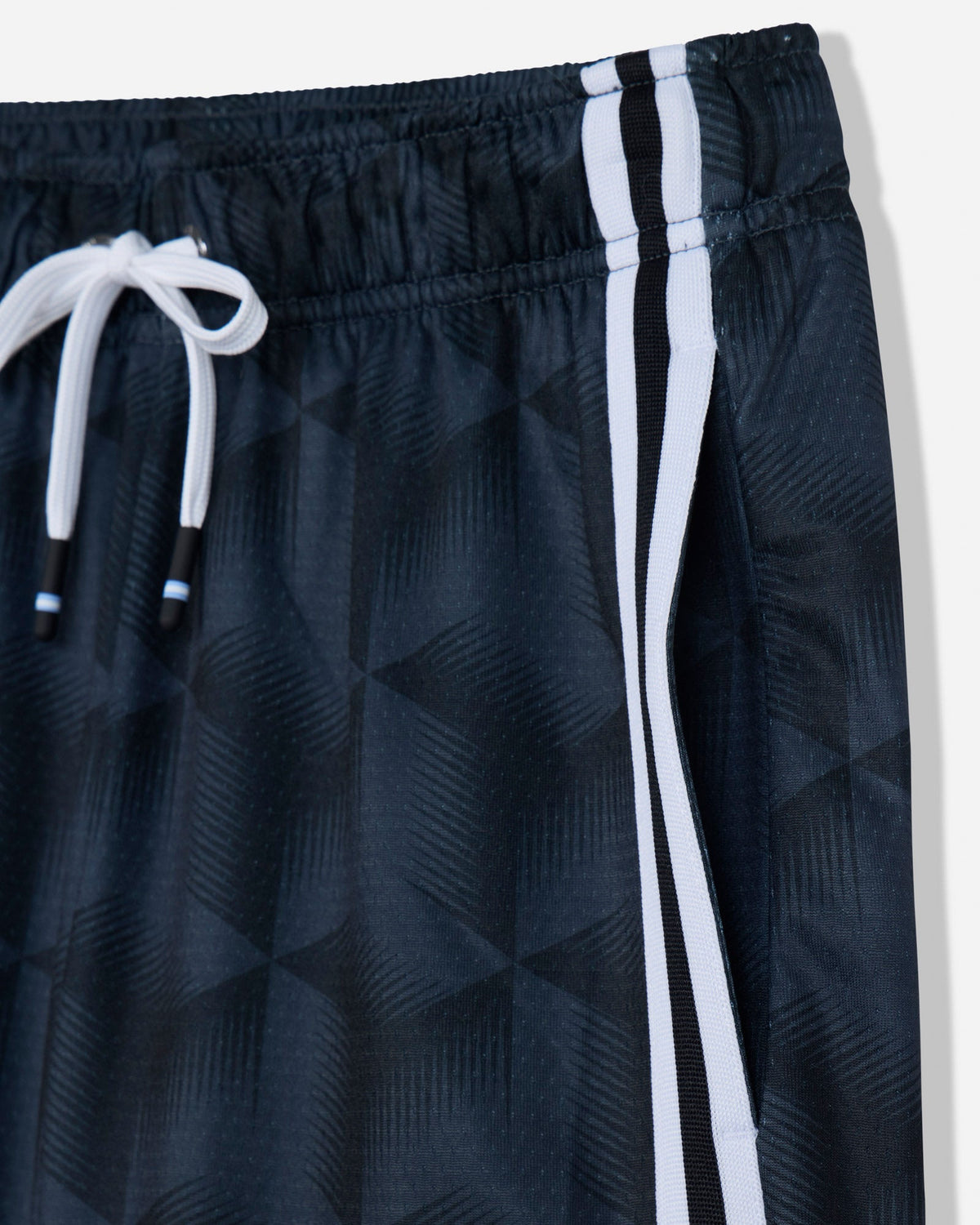 Close-up of dark athletic shorts with a subtle geometric pattern, featuring a white drawstring and two vertical white stripes along the side.