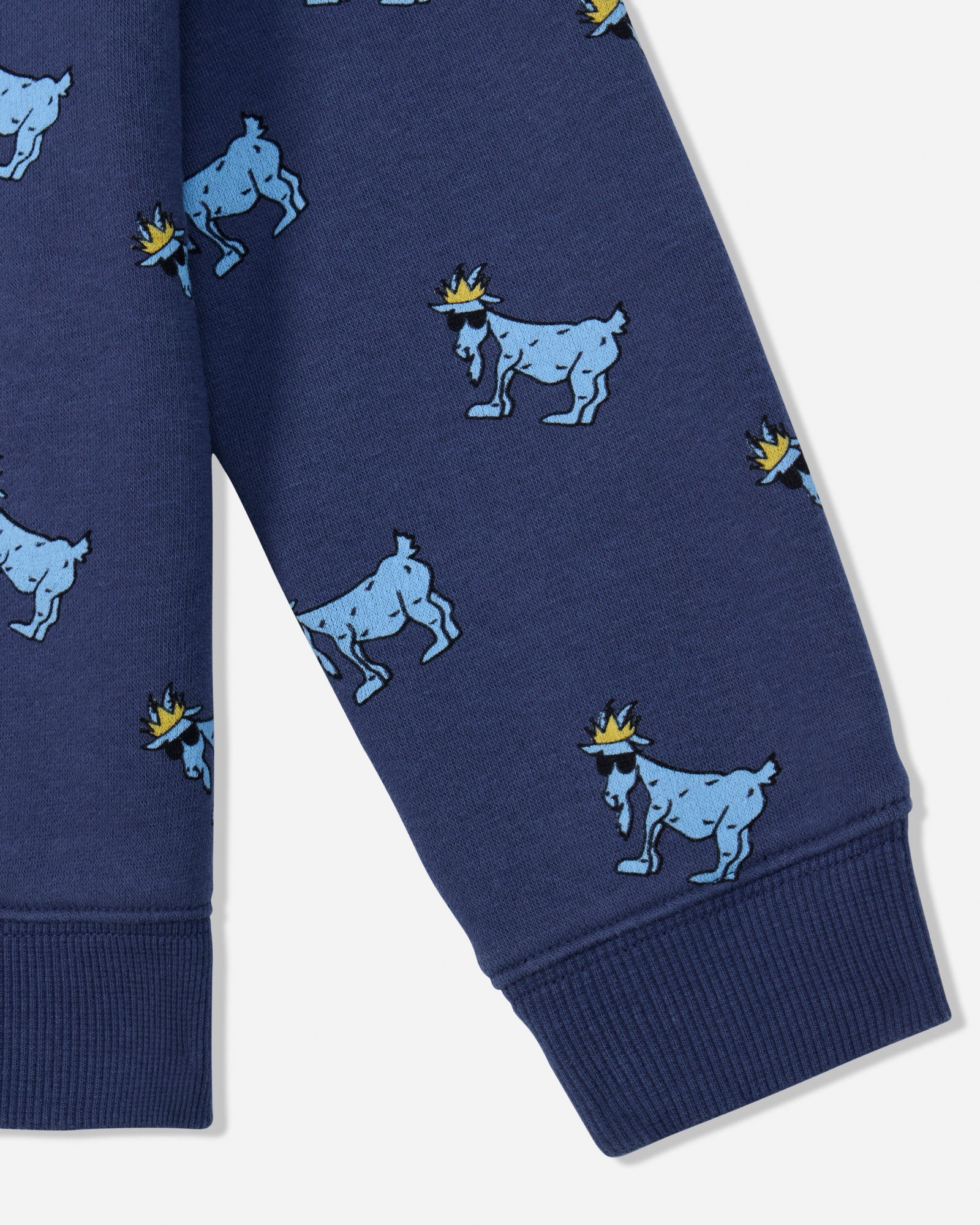 Close-up of a navy blue garment, likely a sweatshirt or pants leg, featuring an allover print of light blue goats wearing small yellow crowns, with ribbed cuffs at the bottom.#color_navy