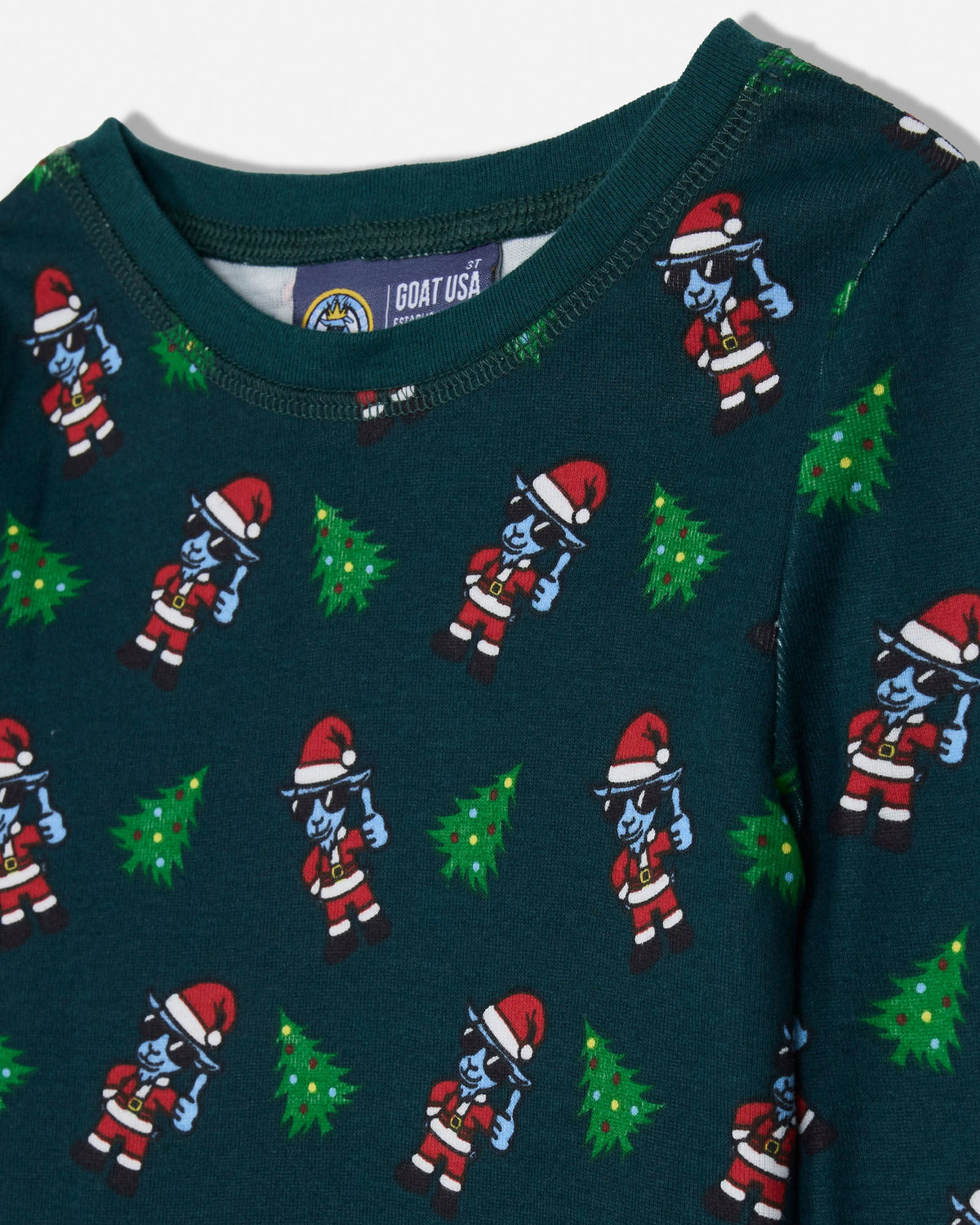 A close-up of a dark teal Christmas-themed long-sleeve top featuring a repeating pattern of cartoon Santa-clad figures and green Christmas trees. The inner neck label shows the brand 'GOAT USA'.