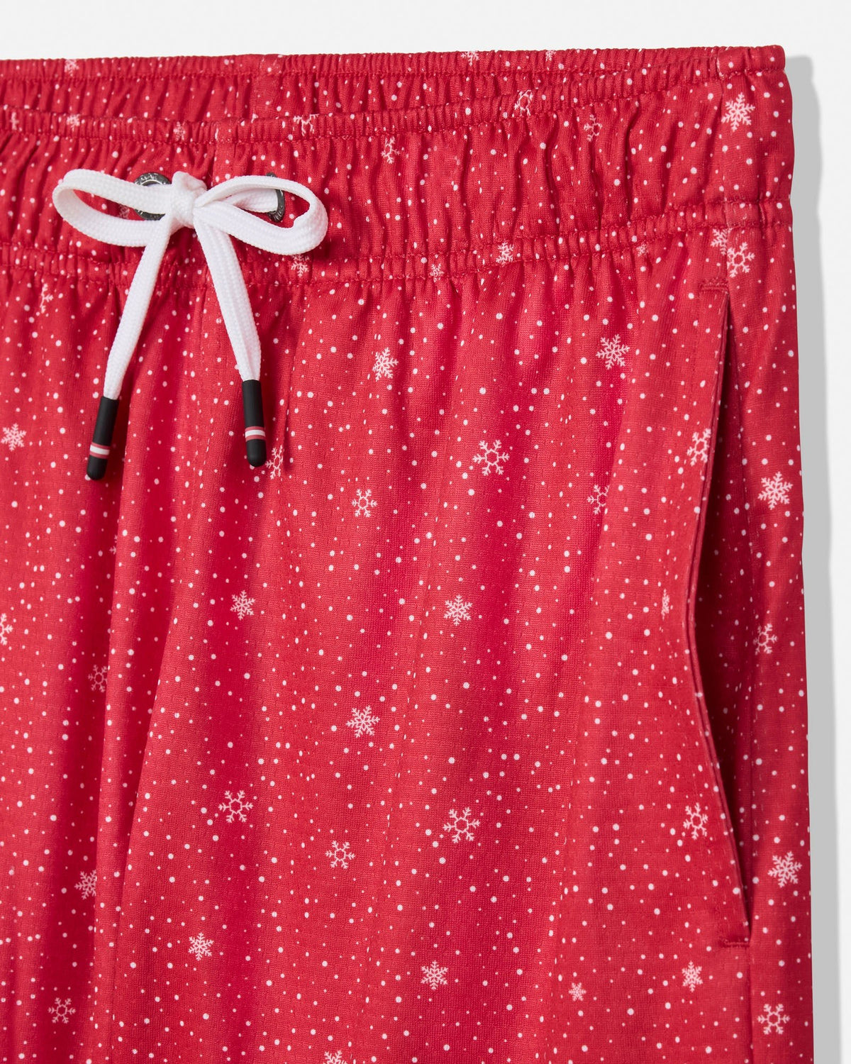 Close-up of red drawstring shorts with an allover white snowflake pattern, featuring a white drawstring tied in a bow at the elastic waistband.