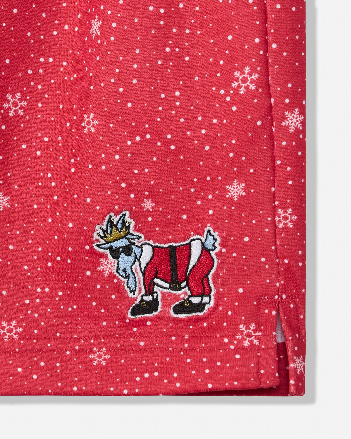 Close-up of a red fabric product, likely a towel or blanket, featuring a white snowflake and polka dot pattern and an embroidered cartoon goat wearing a red and white outfit with a gold crown.