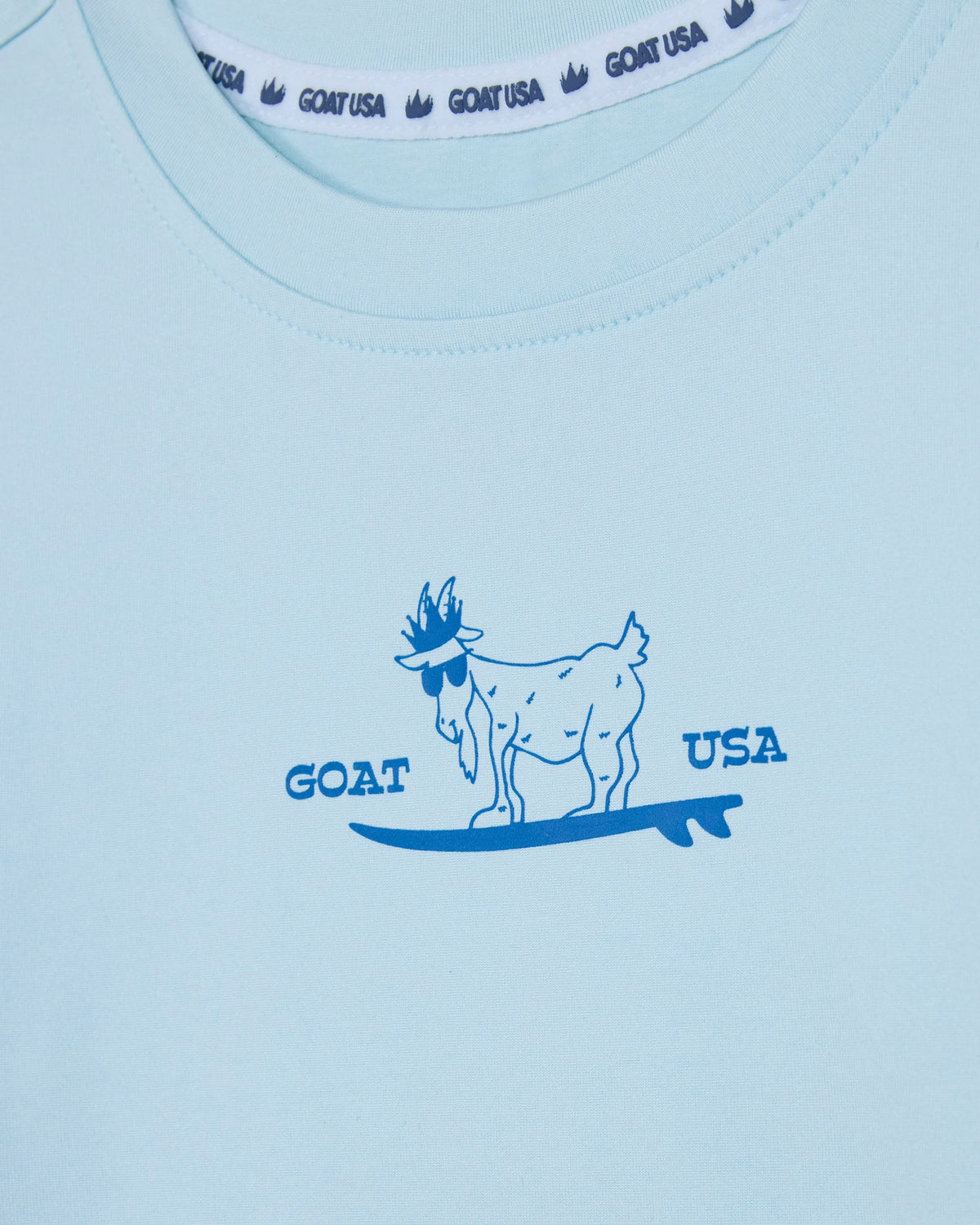 Light blue shirt with a goat surfing graphic and 'GOAT USA' text on a white background