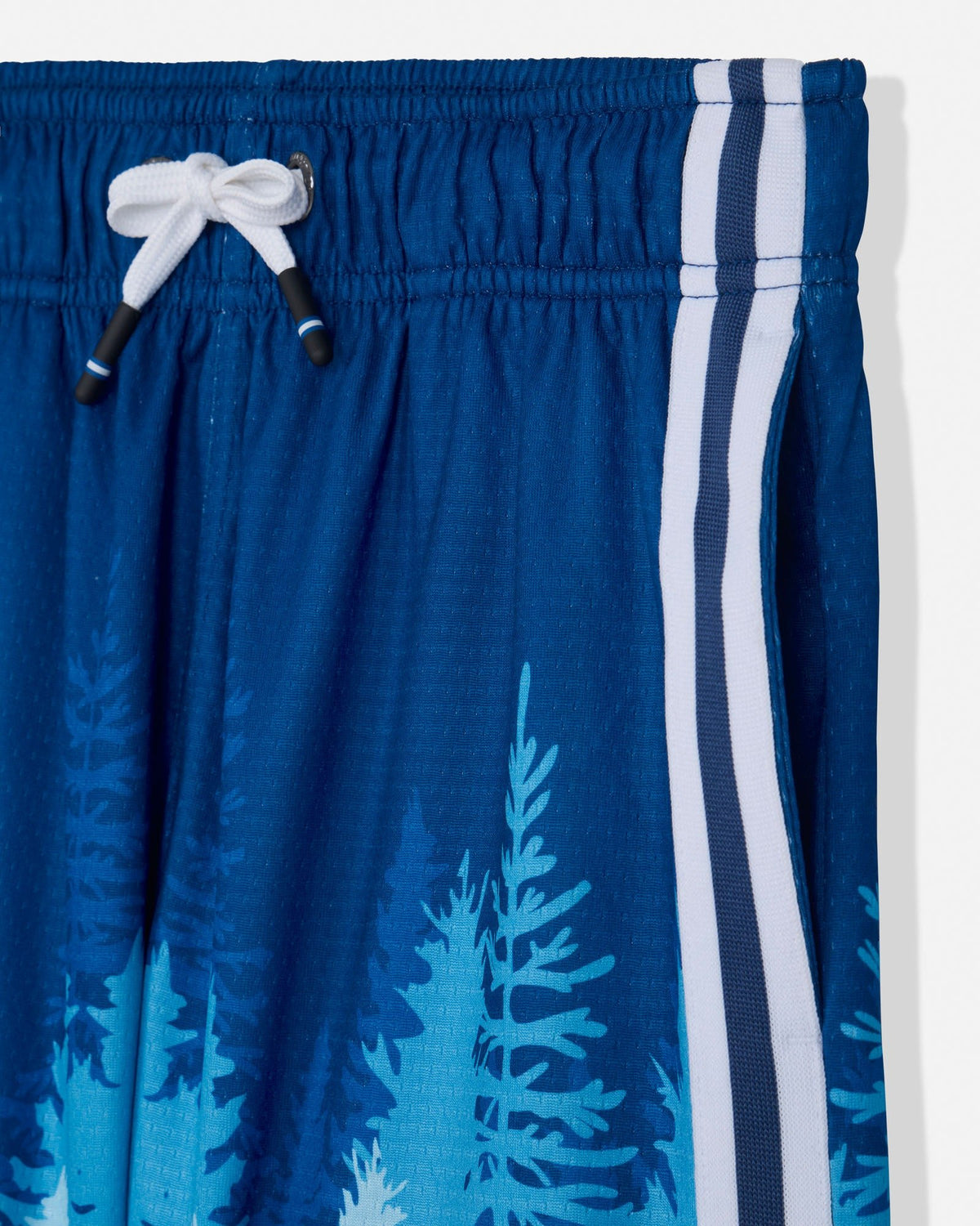 Close-up of blue athletic shorts with a white drawstring, white side stripes, and a light blue pine tree print on a white background.