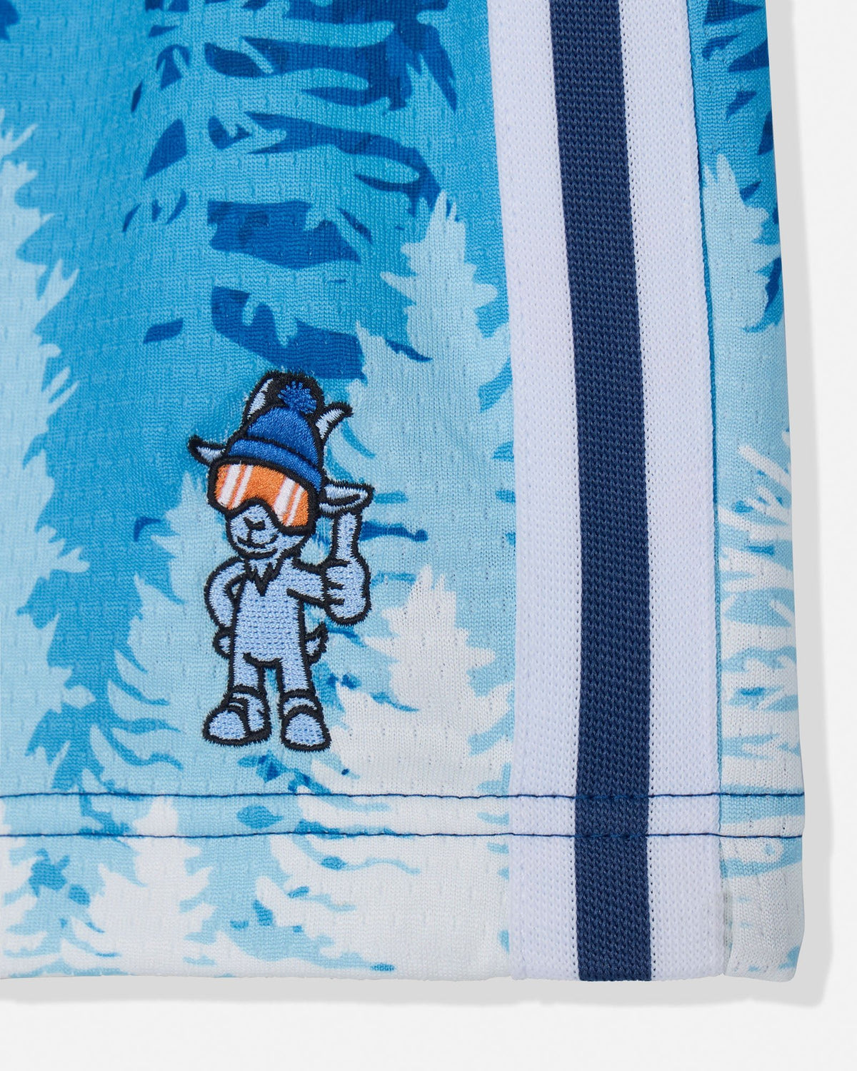 Close-up of blue and white mesh shorts with stripe and pine tree pattern featuring a blue goat holding a thumbs up pose while wearing a winter hat and ski goggles