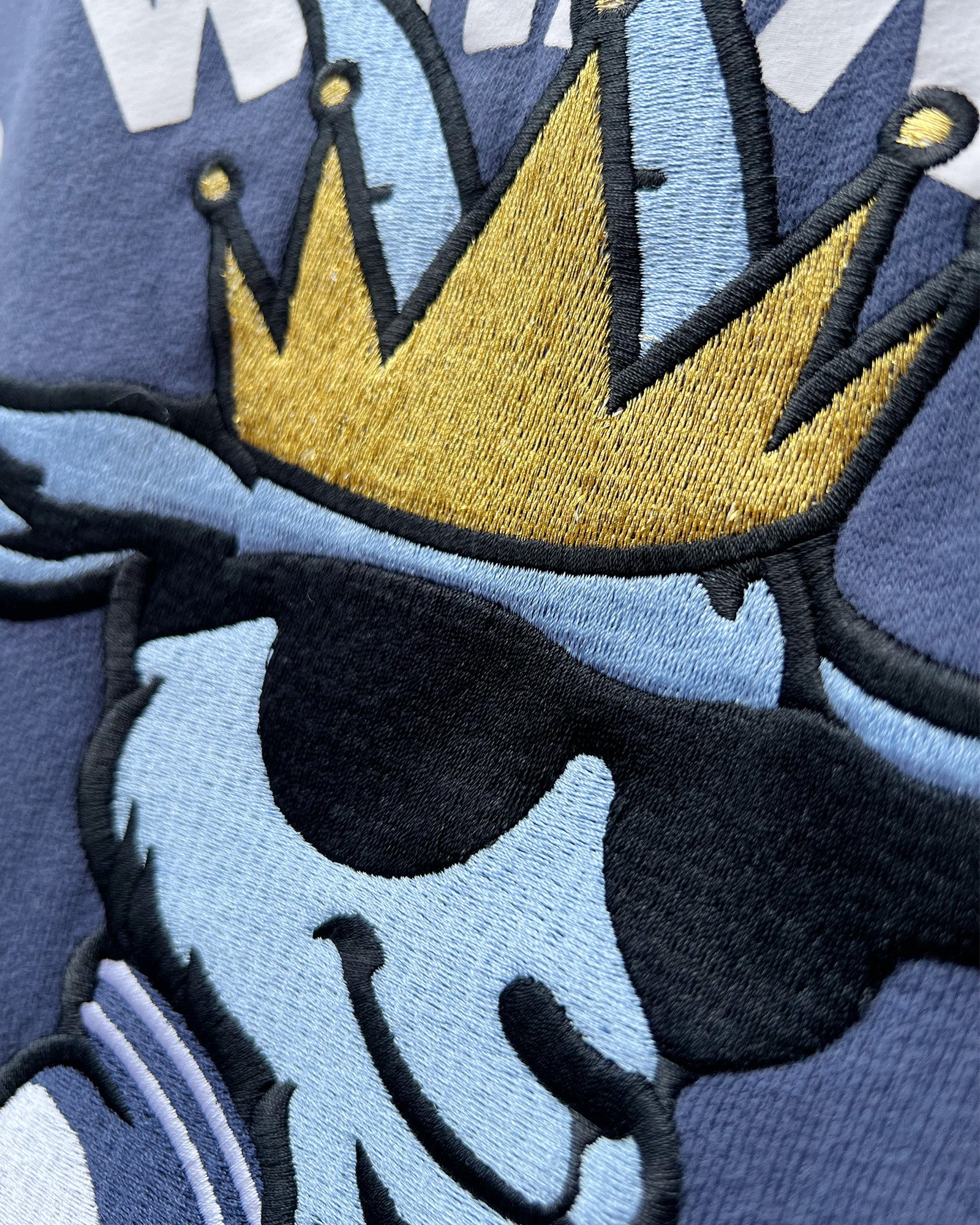Embroidered design of a gold crown on a blue goat