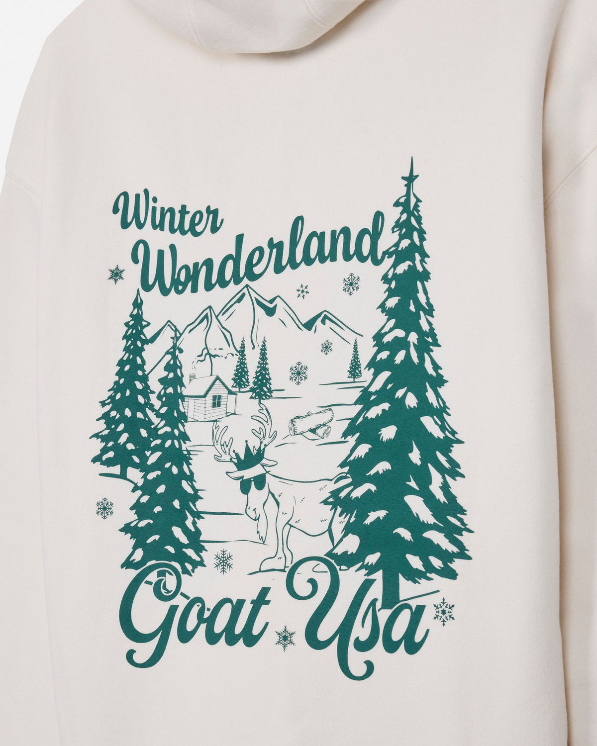 Close-up of a cream-colored hoodie featuring a dark teal graphic print on the front. The graphic depicts a winter landscape with mountains, pine trees, a cabin, a reindeer, and the text 'Winter Wonderland Goat USA'.