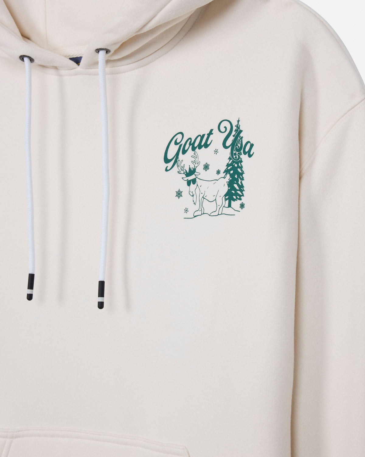Close-up of a cream-colored hoodie with white drawstrings and a green graphic on the left chest featuring the text 'Goat Usa' and a tree illustration.