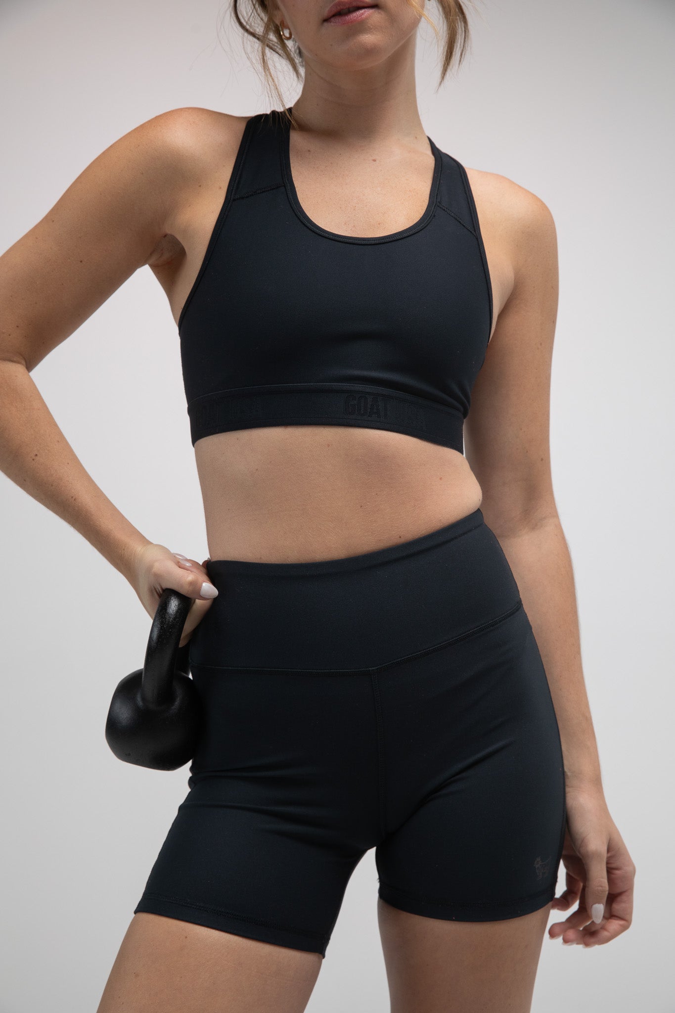 Person wearing bike short and sports bra standing against a gray background