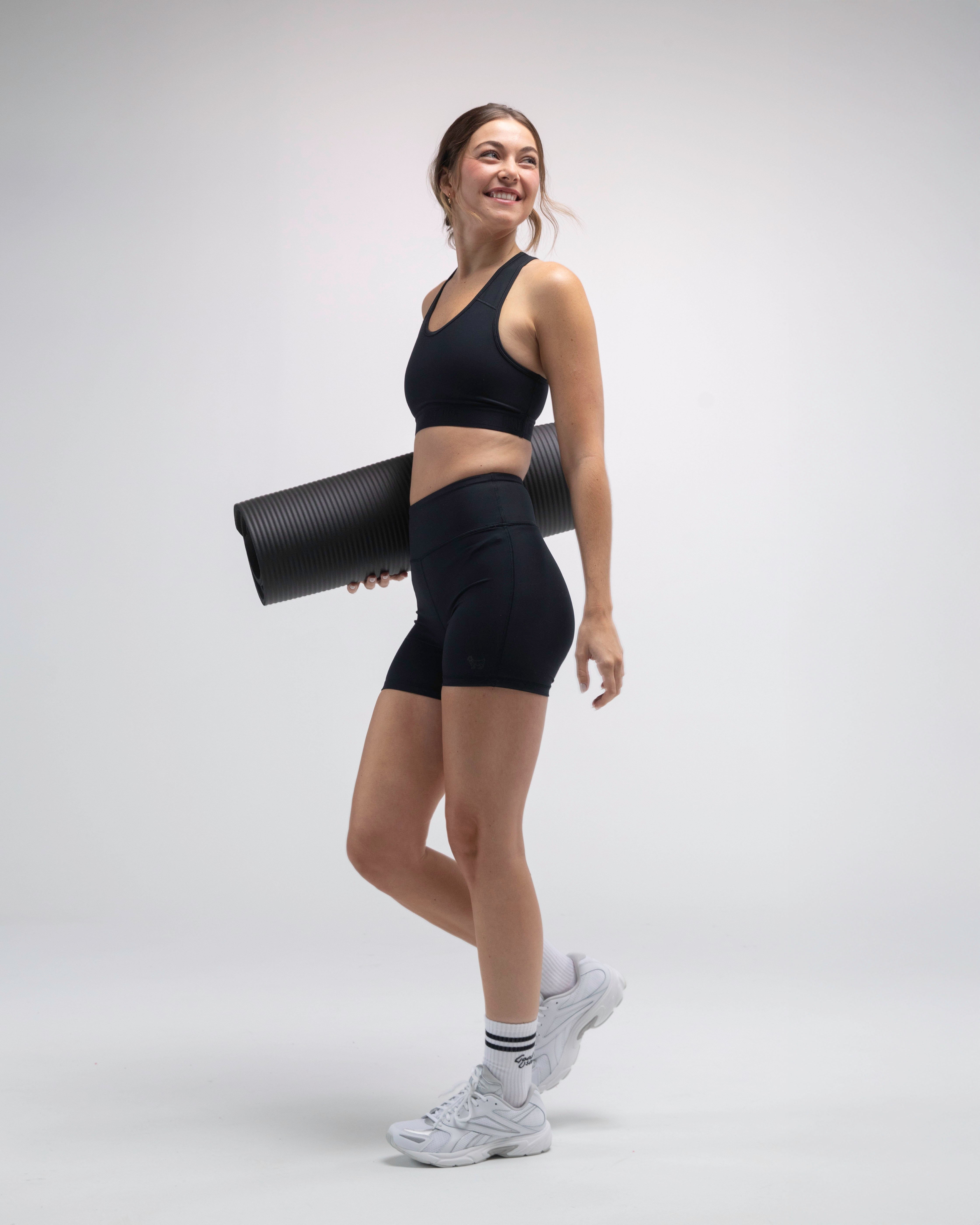 Person wearing bike shorts and sports bra holding a yoga mat