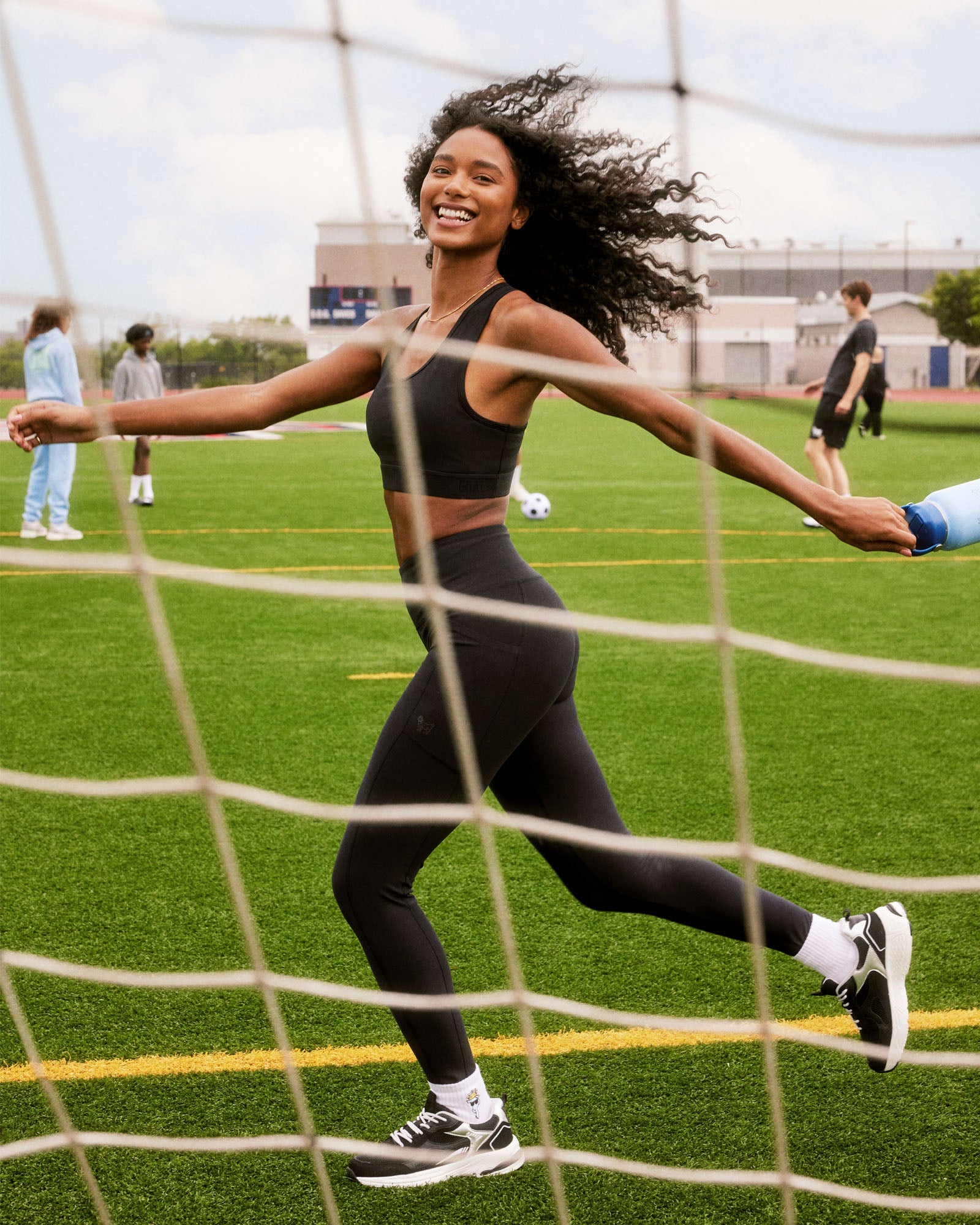 Woman in athletic wear running on a sports field with a goal net in the foreground.