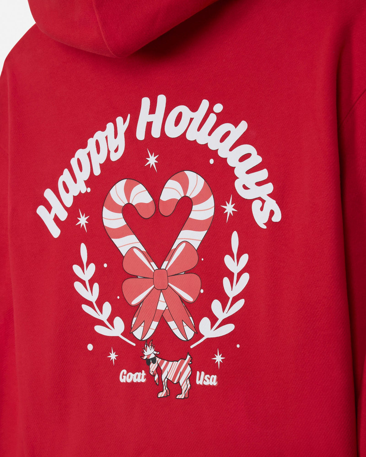 A close-up of a red hoodie showing the back graphic with 'Happy Holidays' in white script, a candy cane and bow motif, white leafy branches, and a small goat with 'Goat USA' text.