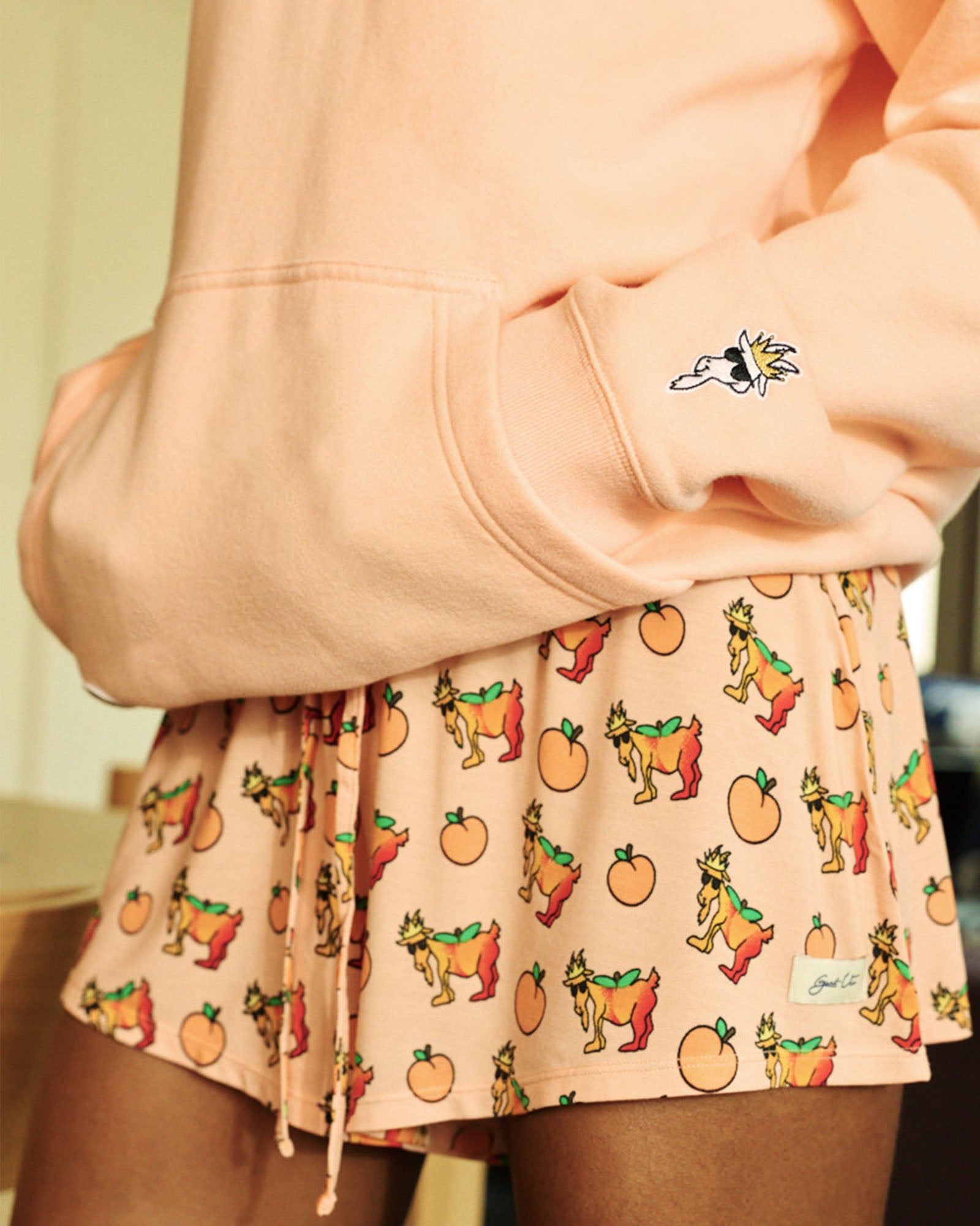 Person wearing a peach-colored hoodie and shorts with a cartoon goat pattern.