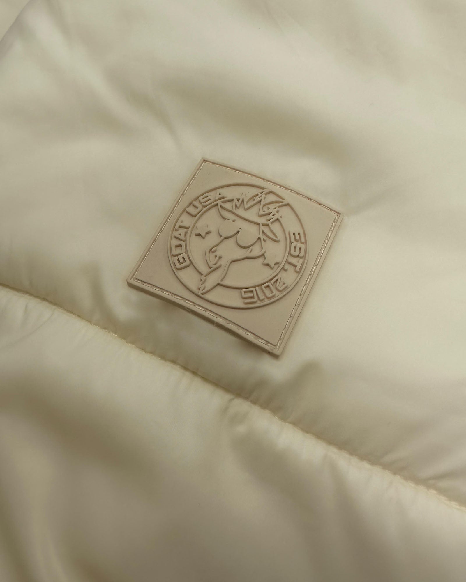 Close up of patch on ivory Women's Puffer Jacket#color_ivory