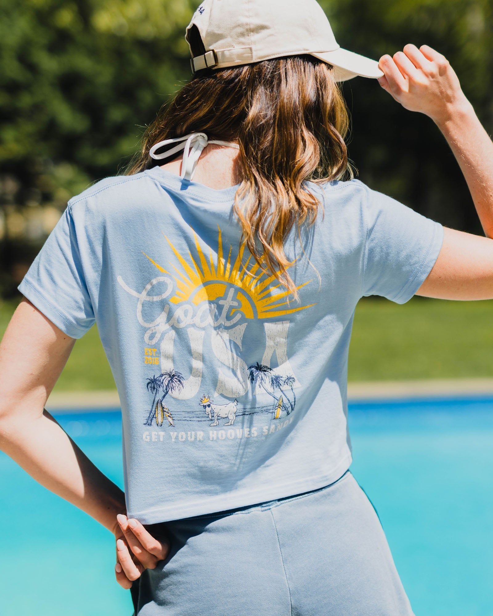 Person wearing a light blue crop top with a graphic design outdoors by a pool