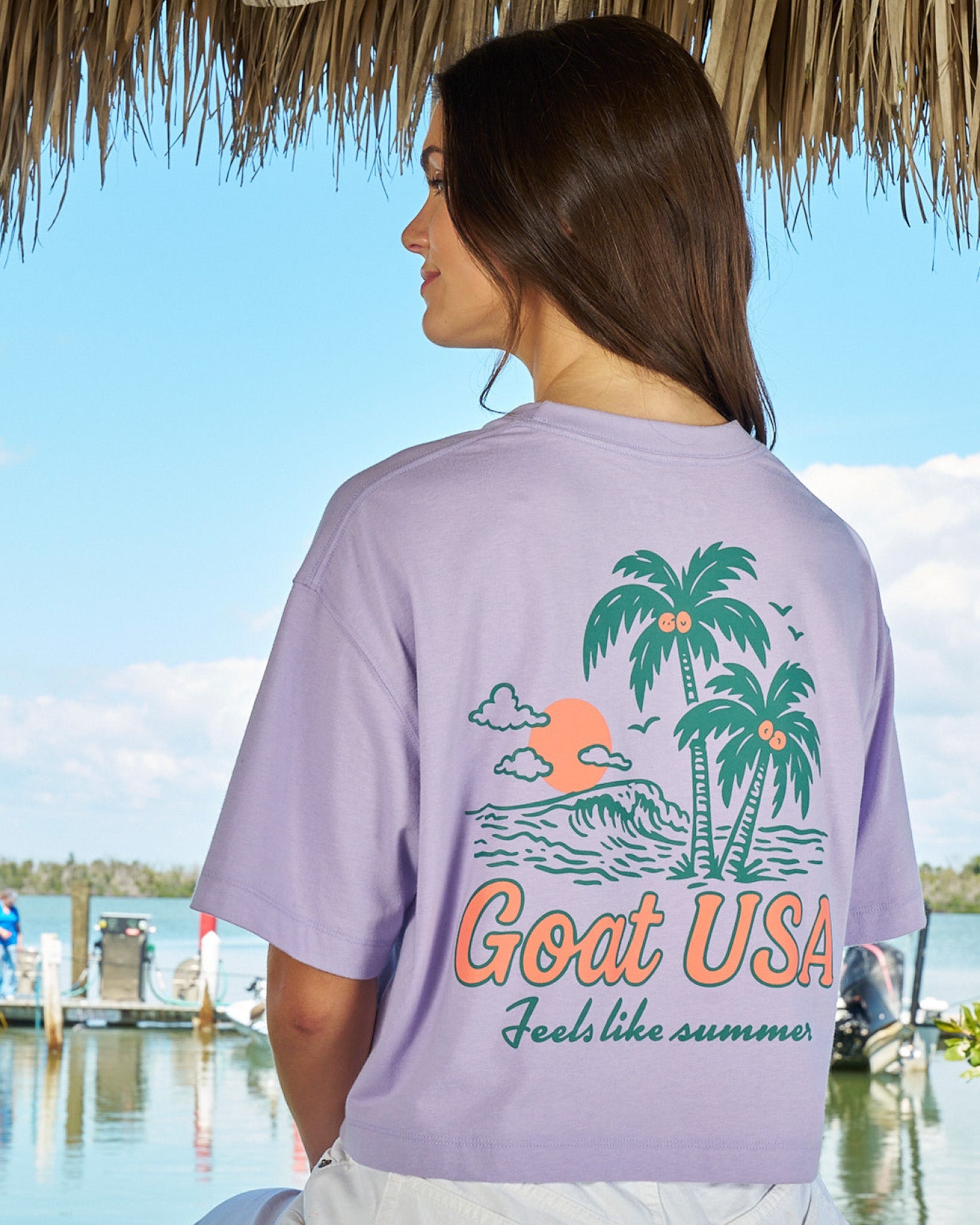 Girl wearing a purple top with palm tree design with water and a dock in the background