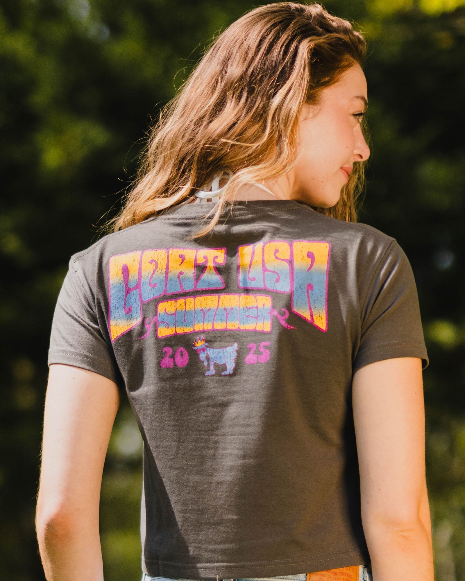 Person wearing a t-shirt with 'GOAT USA' text on the back, standing outdoors.