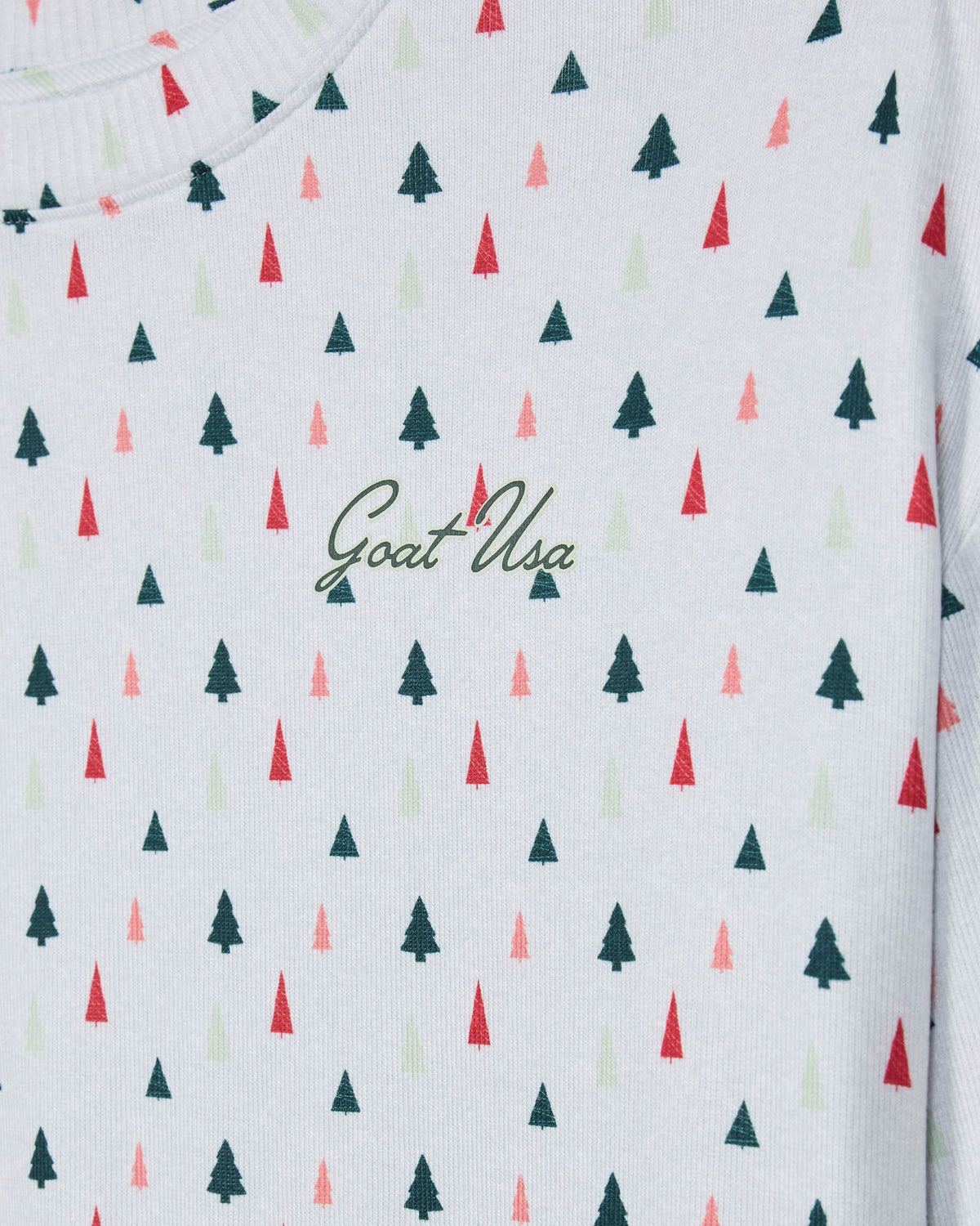Close-up of a white knit garment with a repeating pattern of small pine trees in dark green, red, and pale pink, plus a dark green 'Goat USA' script logo across the chest.