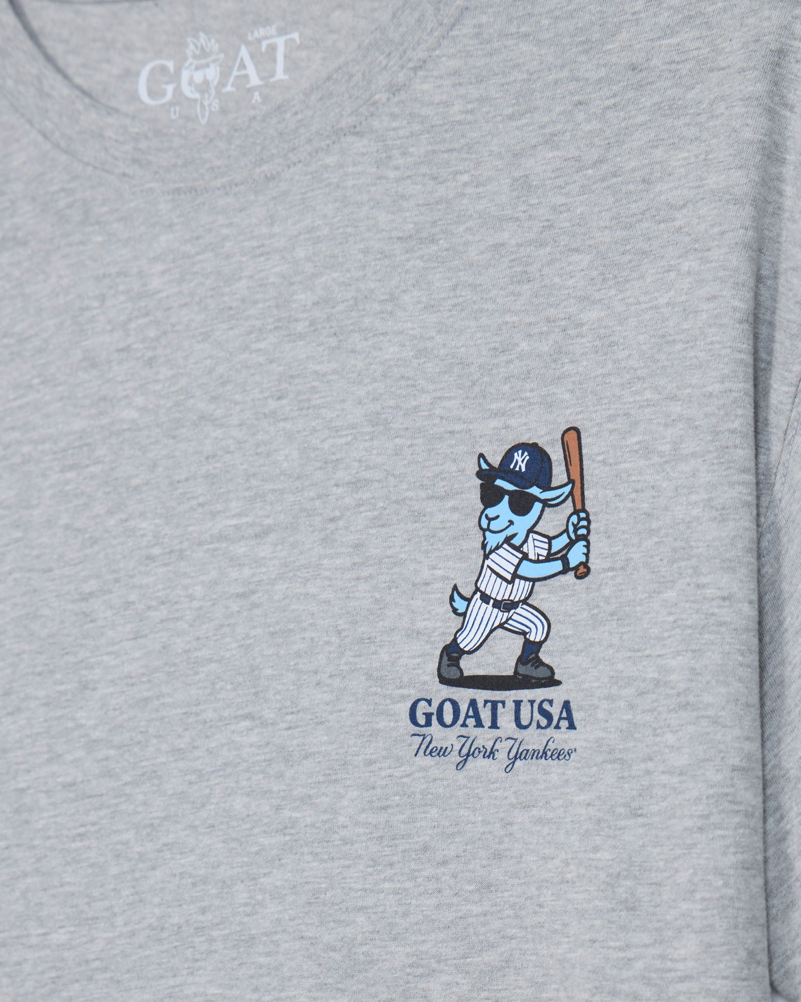 Close-up of a heather gray t-shirt featuring a graphic of a blue and white goat baseball player holding a bat, with 'GOAT USA New York Yankees' printed below.#color_gray