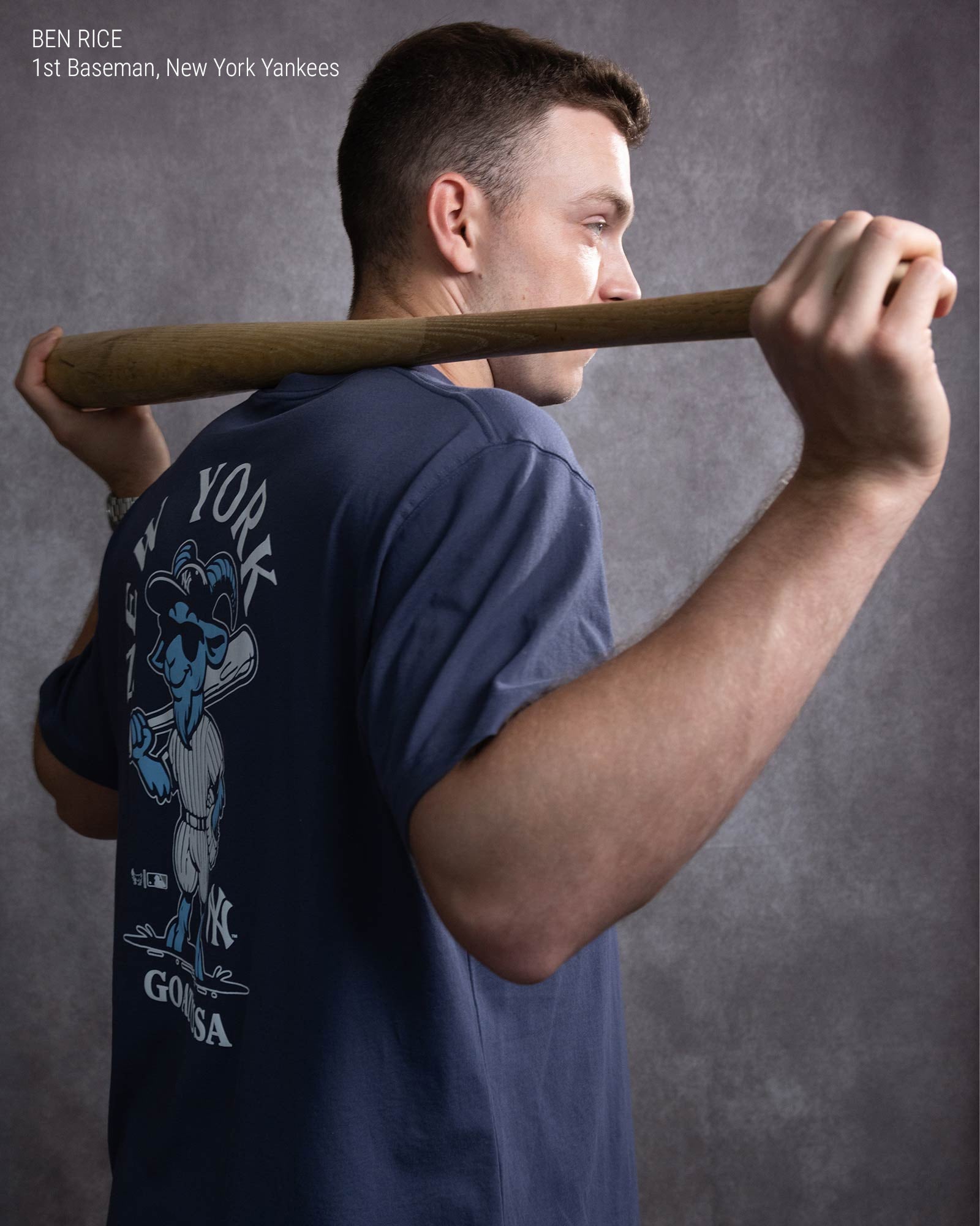 A man holding a baseball bat across his shoulders against a textured gray studio background